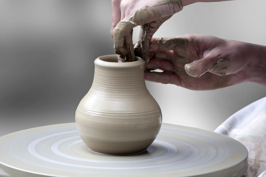 A close up of hands moulding a small vase of pottery on a wheel